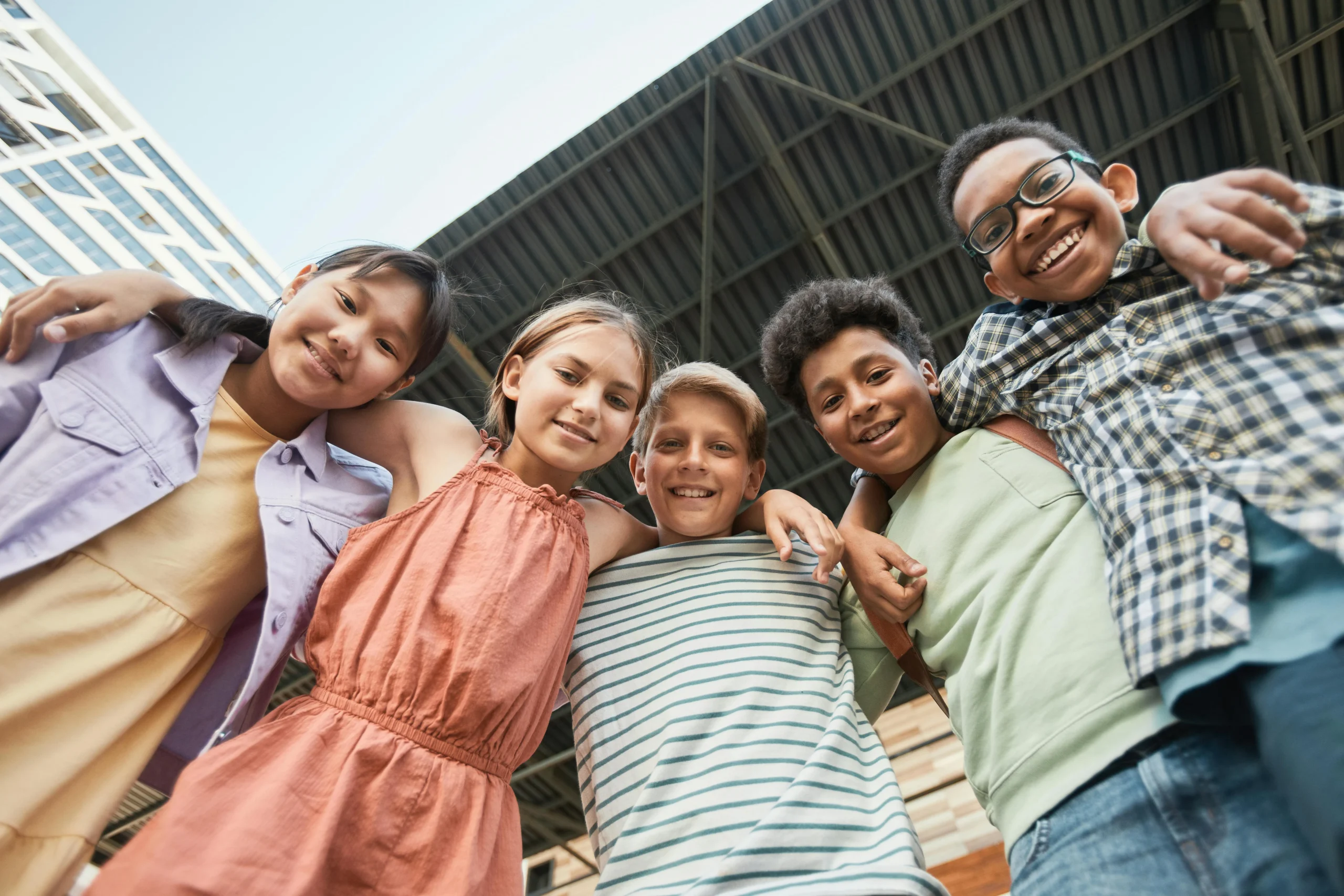 a group of kids looking down towards the ground, smiling together.