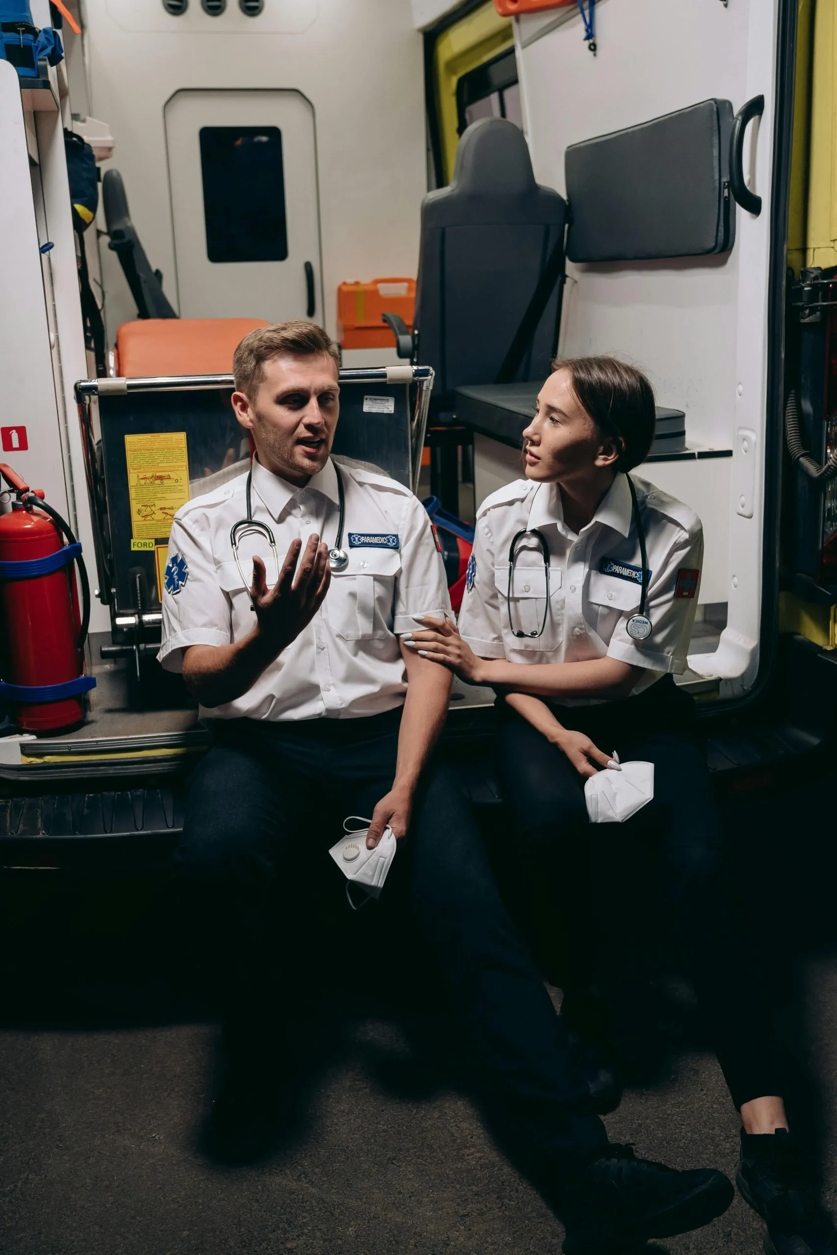 Male and female paramedics talking on the back of their truck.